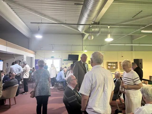 A crowd of people inside a bowling club, sitting or standing in groups