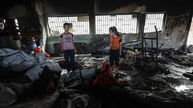 A young boy and a girl stand in what used to be the Musa bin Nasir School where Palestinians took shelter before Israel bombed it. the walls are blackened and debris is everywhere