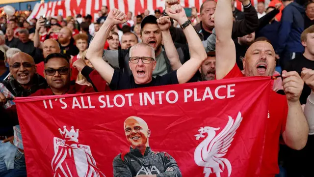 Liverpool fan displays a flag which reads "It's all Slot into place"