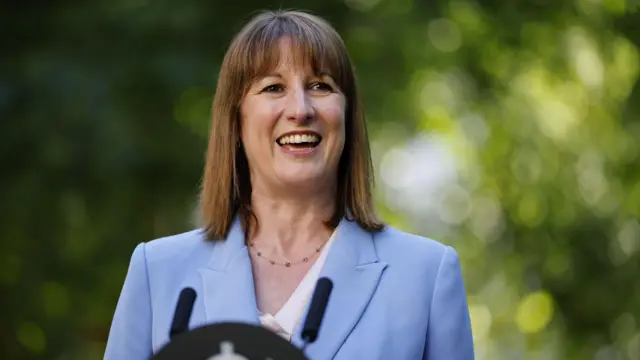 Reeves speaking at ceremony, smiling in front of a microphone