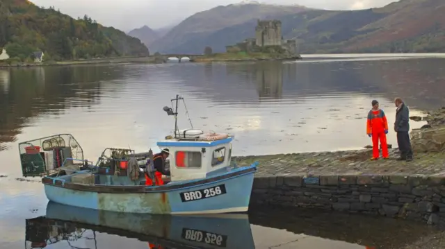 A fishing boat sits on a lake, with a small mountain in the background