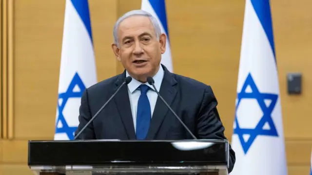 Israeli Prime Minister Benjamin Netanyahu speaks behind a podium with Israeli flags in the background.