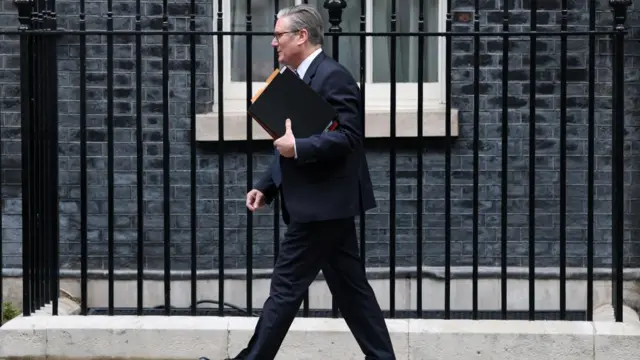 Keir Starmer walks down a street past a metal fence.