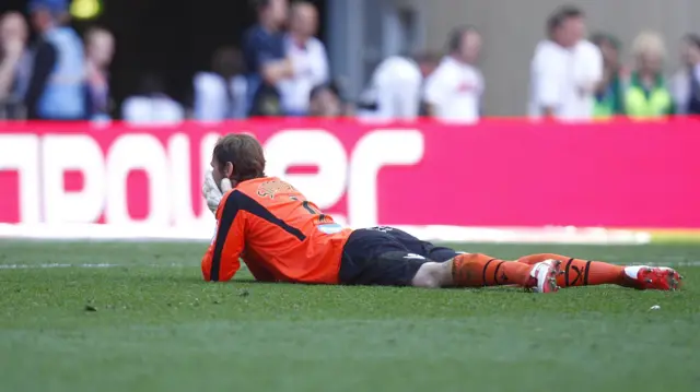 A goalkeeper in orange kit holds his face in anguish