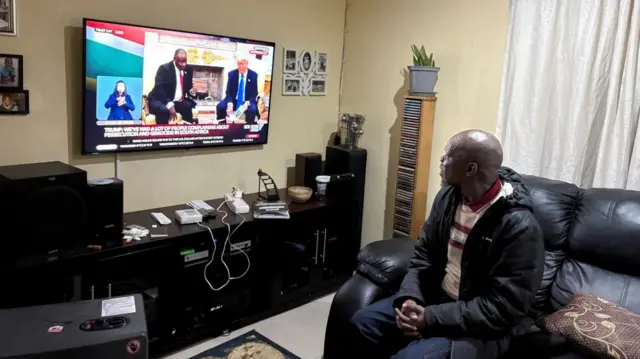 watches on his television set as U.S. President Donald Trump confronts South African President Cyril Ramaphosa at the White House