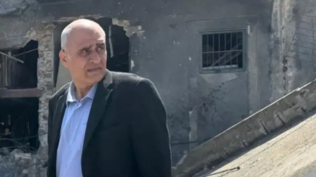 Amjad Shawa standing in front of a building in ruins