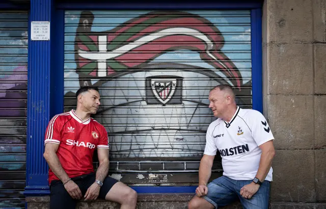 United and Spurs fans sit opposite one another on a ledge