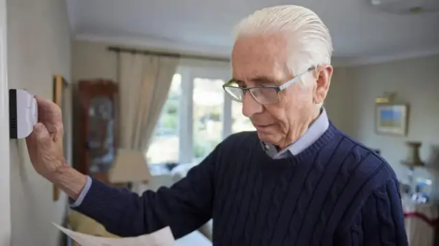 An older looking man adjusts the heating in the room.