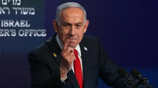 Benjamin Netanyahu wears a suit and red tie and points his finger at a press conference in Jerusalem.