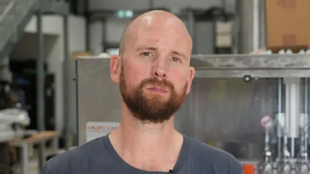 James Sander looks directly in the camera with the backdrop of a brewery