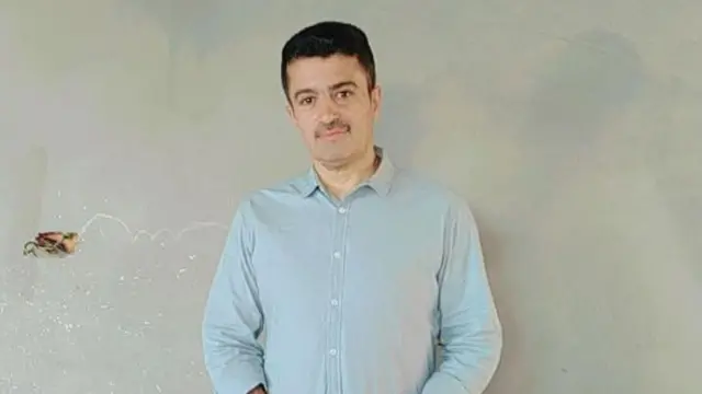 A Palestinian man stands looking at the camera wearing a collared shirt.