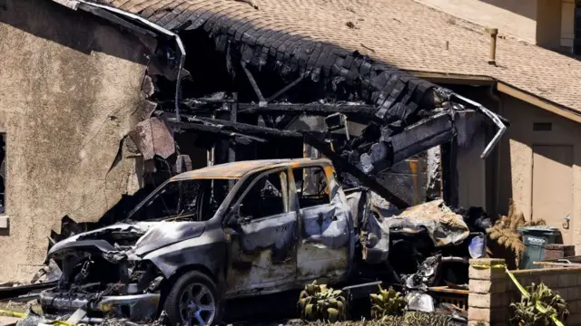A burnt out car in the middle of a destroyed home