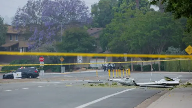 Parts of a small civilian aircraft on the road with police cordons around it