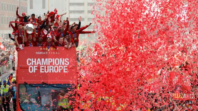 Liverpool players hold the Champions League trophy aloft in 2019 from an open top bus in front of fans
