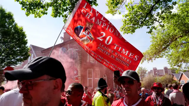 Liverpool fans gather and wave a flag as they await the arrival of the team coach ahead of the Premier League match at Anfield, Liverpool.
