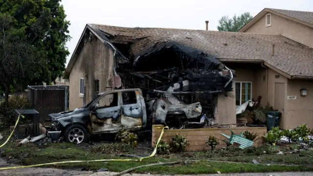 A house with a massive burnt out hole in its side and a burnt out car