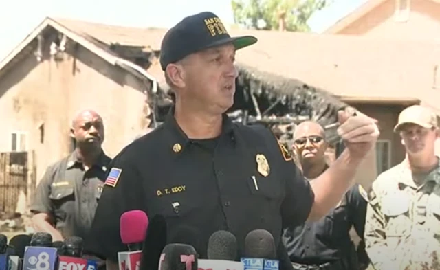 Eddy speaking in front of a damaged house