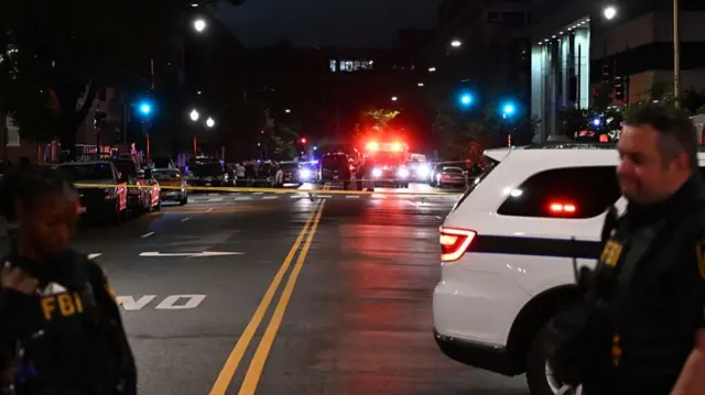 Emergency vehicles are seen in the distance as FBI agents guard the scene outside the Capital Jewish Museum following a shooting