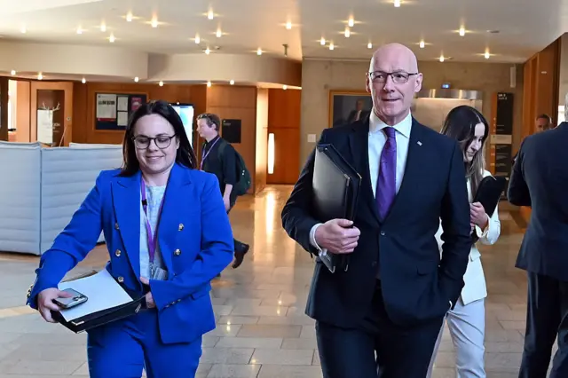 Kate Forbes in a blue suit and john swinney in a dark suit with a white shirt and purple tie walking through the Holyrood building