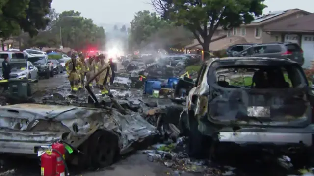 Two burnt out cars, one flattened, on a suburban street