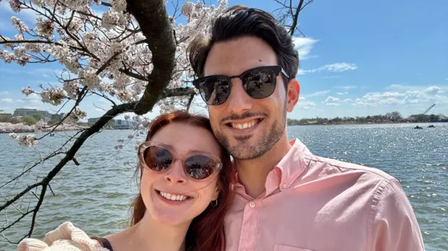 Sarah Miligrim and Yaron Lischinsky take a selfie in front of a body of water in the sun