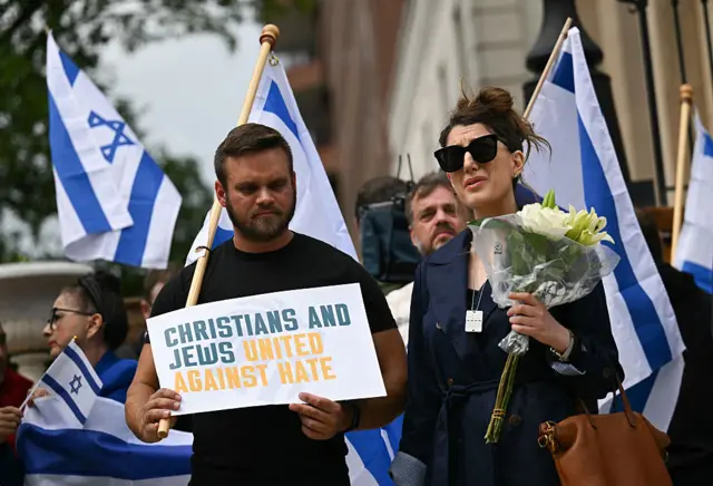 People hold signs and Israeli national flags in a sign of support outside the Capital Jewish Museum. One sign says: Christians and Jews United Against Hate.