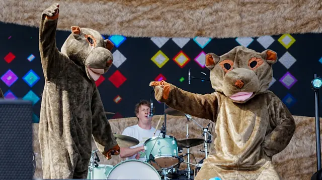 Two dancers dressed as wombats dance on the Main Stage at Radio 1's Big Weekend in front of a drummer playing on the drums.