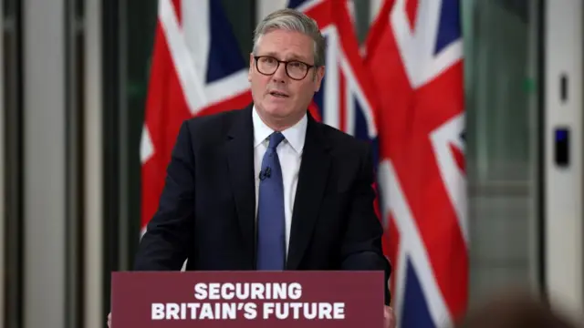 Starmer stood behind podium saying Securing Britain's Future, with UK flag behind him.