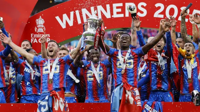 Joel Ward and Marc Guehi lift the FA Cup, surrounded by their team-mates, after Crystal Palace win the 2025 final