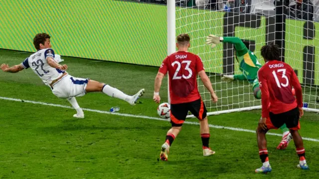 Tottenham's Brennan Johnson (L) scores the 1-0 goal against Manchester United. Man U left-back Luke Shaw and wing-back Patrick Dorgu in red uniforms stand in front of the goal as goalkeeper Andre Onana dives for the ball