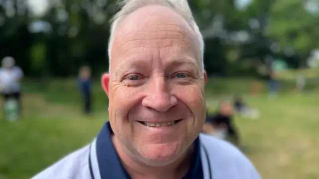 Daryl Rowlands is seen from the shoulders up smiling directly at the camera. He is wearing a Spurs polo-shirt.