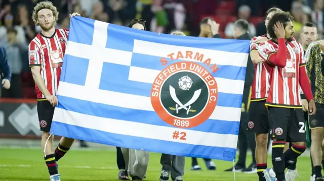 Sheffield United players carry a large Greek blue and white flag with horizontal lines with the legend Starman written above a Sheffield United crest