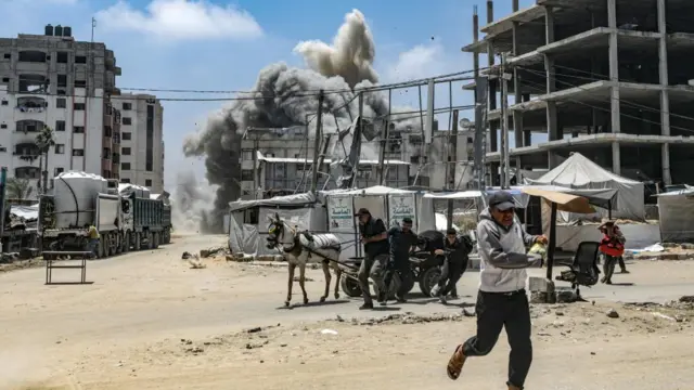 A Palestinian man runs for cover in Gaza City. Plumes of smoke can be seen in the background.