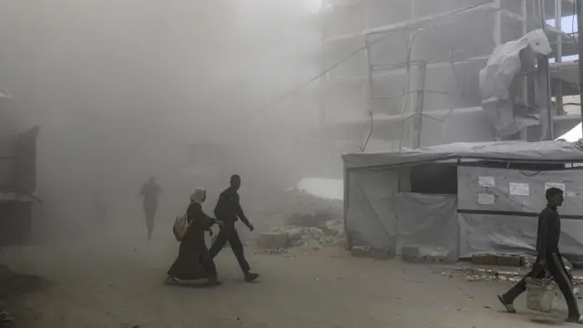 A man and a woman walking on a road in Gaza city amid a haze of smoke.