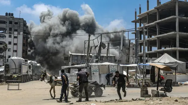 Palestinians run for cover as smoke rises following an Israeli airstrike west of Gaza City