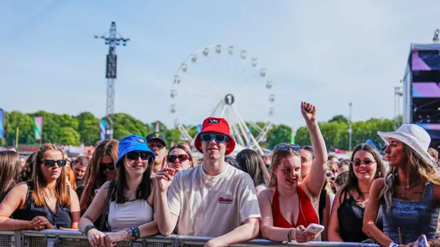 Several festivalgoers watch Bedingfield perform on the main stage. There's a ferris wheel in the background.