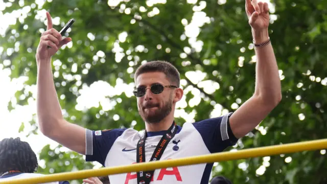 Guglielmo Vicario is seen on top of the parade bus with his arms up wearing sunglasses