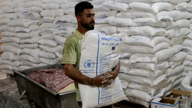 A man carrying a bag of flour with the WFP label on the front unloads flour.