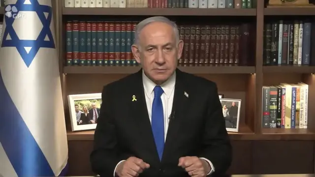 Netanyahu sitting at a desk with an Israel flag behind him to one side