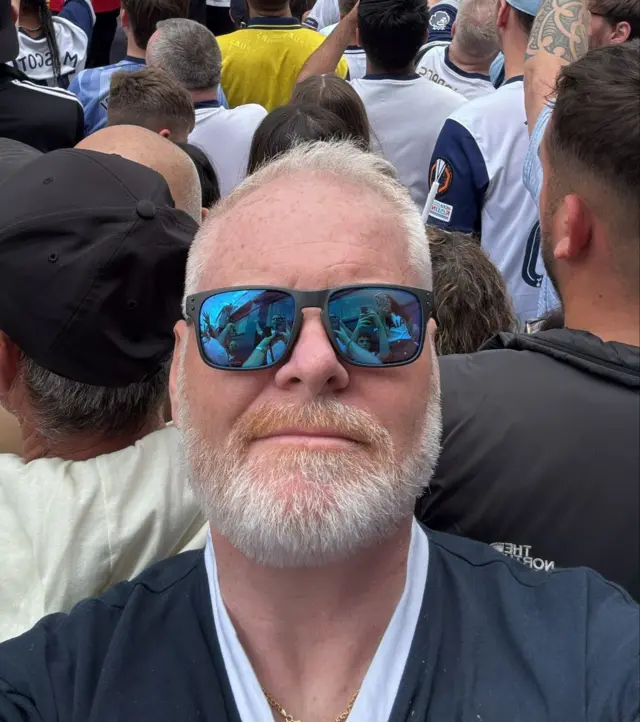 Gary Parker is seen in a selfie wearing sunglasses among the crowds in Tottenham