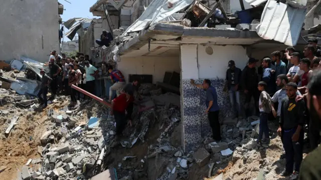 Photo shows what appears to be a house in ruins, with several people crowding around it.
