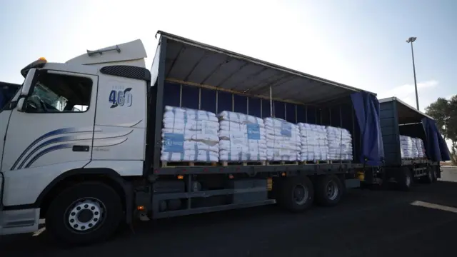 A lorry with its side open and lots of white bags piled up on pallets