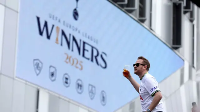 A lone man is pictured holding a beer with a stadium screen stating winners dominating the background.