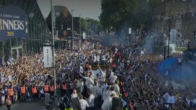 Two open top buses carry Spurs team in front of stadium flanked by thousands of fans either side