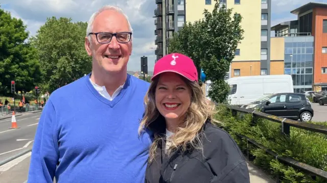 Duncan Brundell and Nancy Corbin are seen smiling at the camera. Nancy is wearing a red Spurs hat.