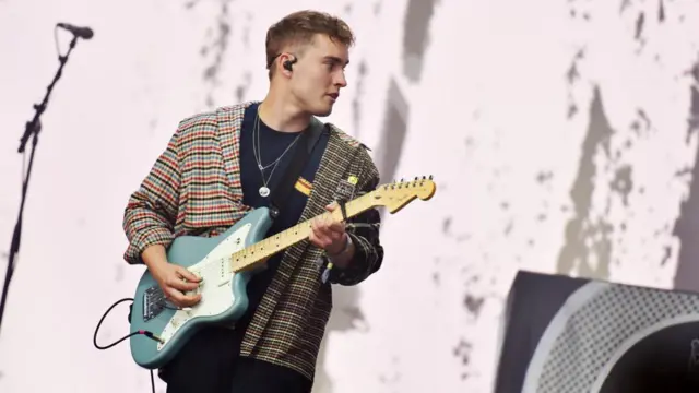 Sam Fender playing guitar in front of a microphone on a stand.