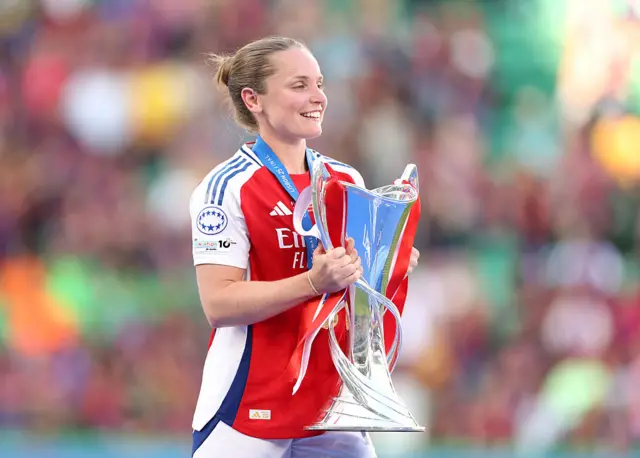 Kim Little carries the trophy over to the podium before lifting it