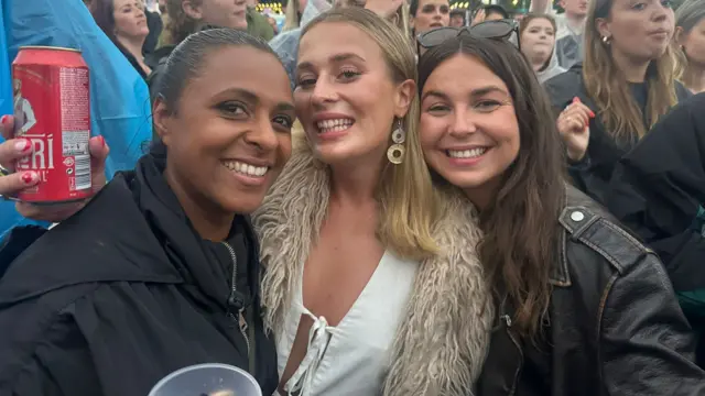 Charlene, Harriet and Lydia pose for the camera while stood in the crowd at Big Weekend's Main Stage. Two of them have brown hair and one has blonde hair. They are all wearing coats.