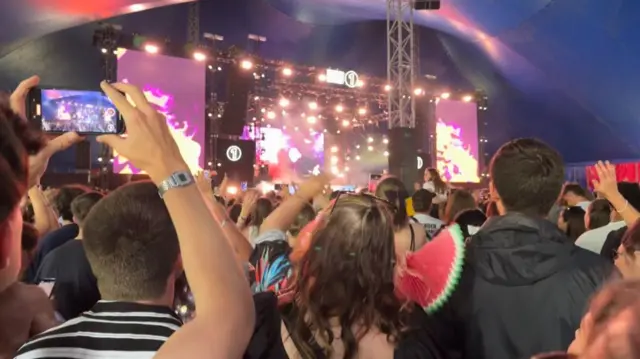 a crowd of people, some holding up their phones to record, watch ed sheeran perform