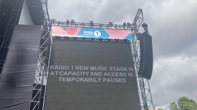 A sign reads: "Radio 1 New Music Stage is at capacity and access is temporarily paused."